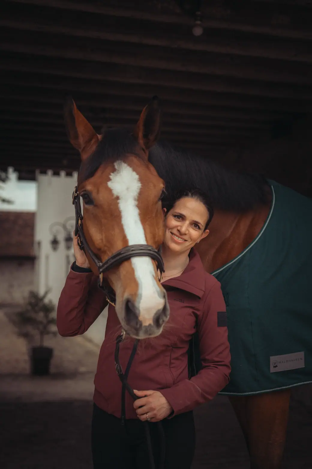 Francesca Hazan standing cheek to cheek with a rugged bay horse in the stable yard.